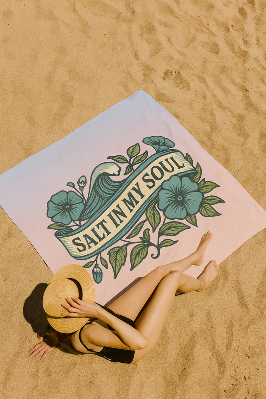 Person lying on a beach with a towel featuring 'Salt in My Soul' text and floral design.