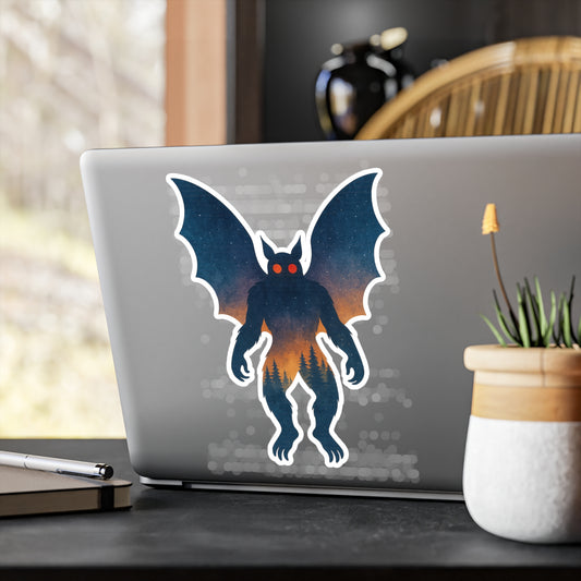 Laptop with mothman creature sticker on a desk with a plant and pen.