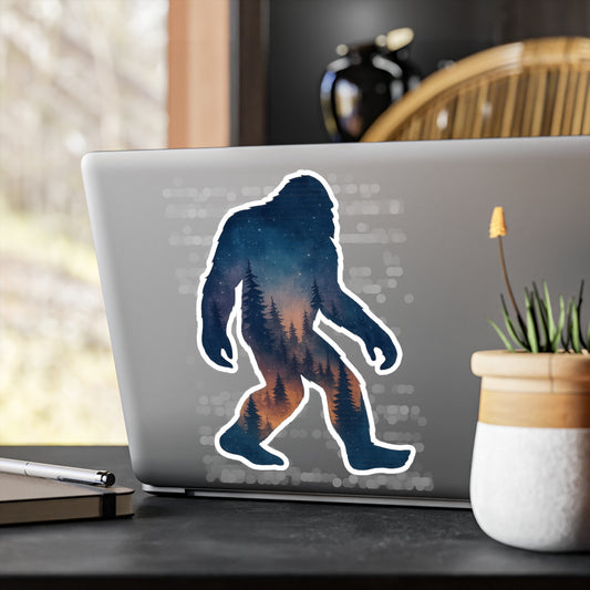 Laptop with a Bigfoot silhouette sticker on a desk with a plant and pen.