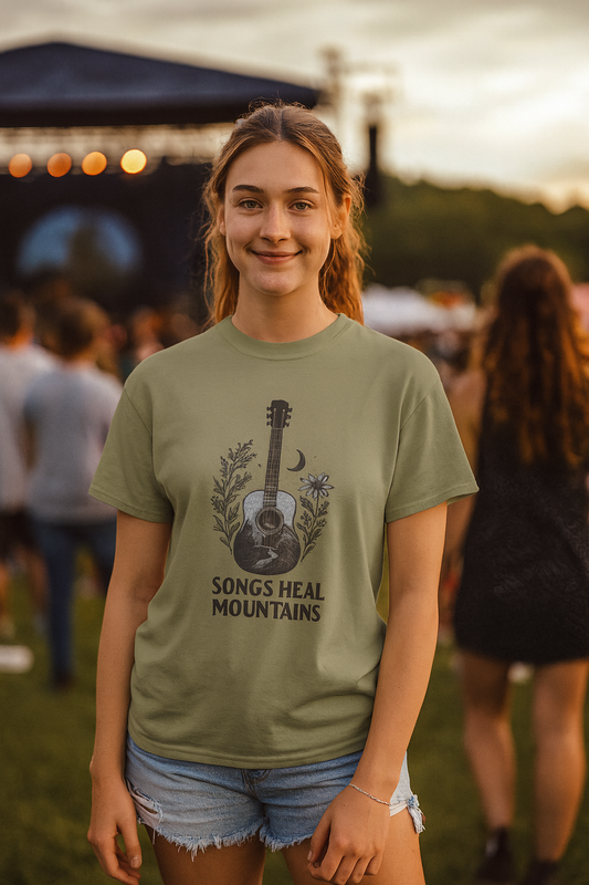 Person wearing a green t-shirt with a guitar and moon and text that says "songs heal mountains", standing in a casual outdoor setting.