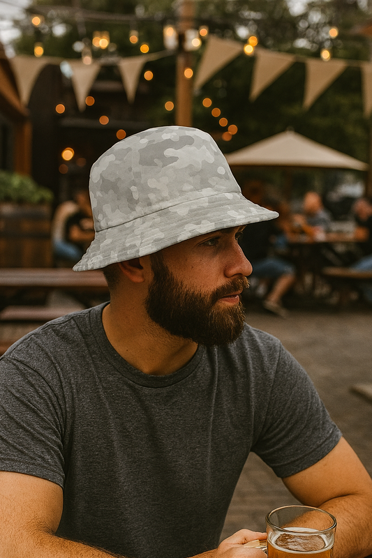 Man sitting at an outdoor table with a beer, wearing a bucket hat and gray t-shirt.