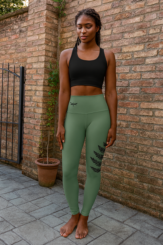 Woman wearing green leggings with a leaf design and black sports bra against a brick wall.