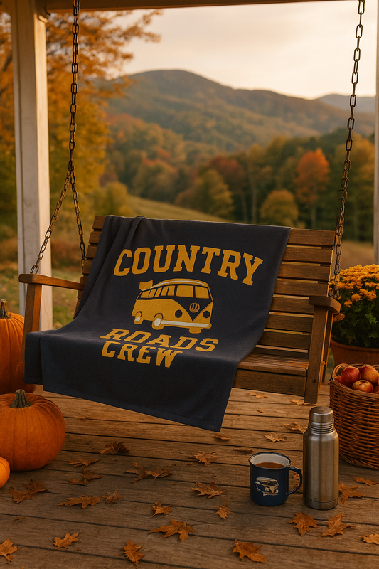 Blanket with 'Country Roads Crew' design on a wooden swing with autumn scenery.