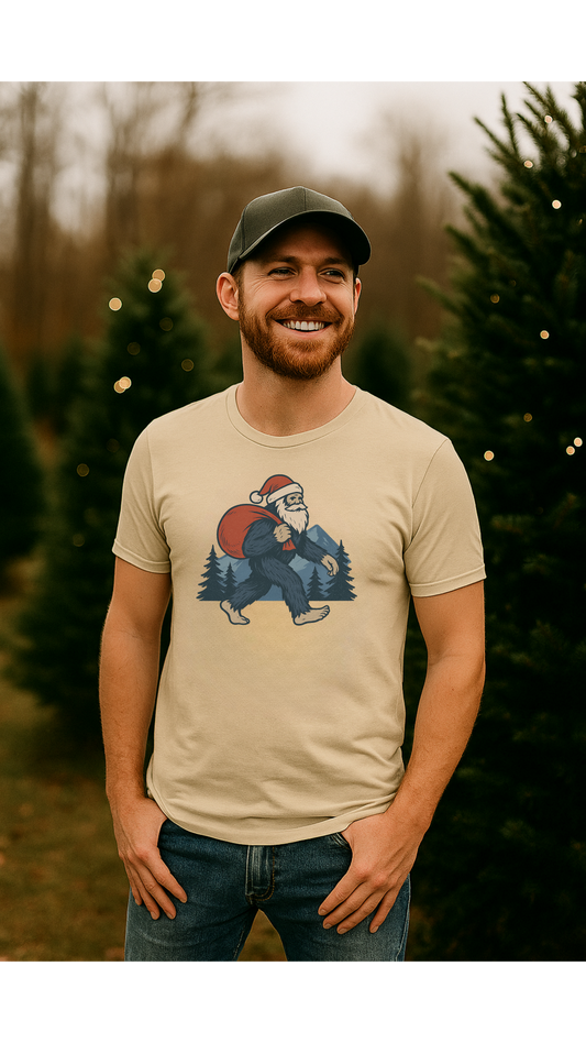 Man wearing a beige t-shirt with a graphic design of a bear wearing a Santa hat and holding a Christmas tree, standing in a Christmas tree lot.