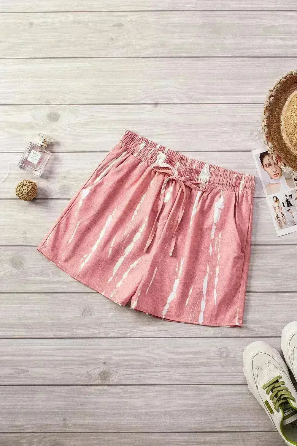 Pink shorts on a wooden surface with a sneaker and decorative items.