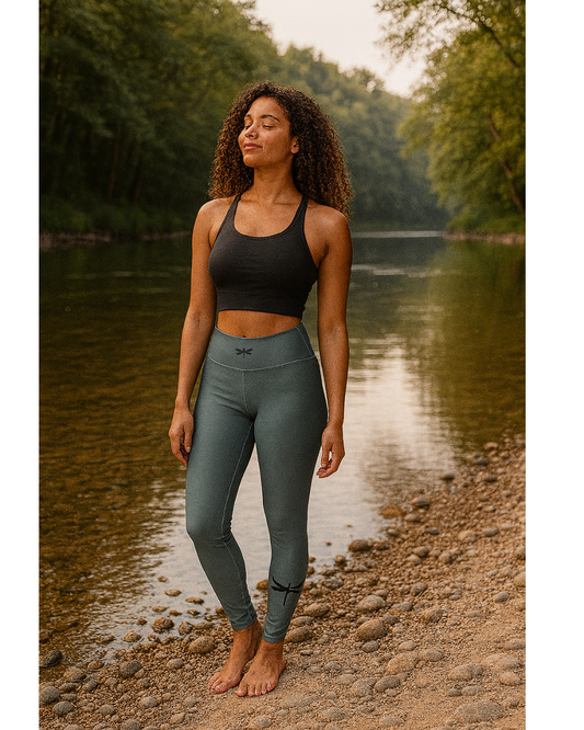 Woman in dragonfly yoga wear standing by a river with trees in the background